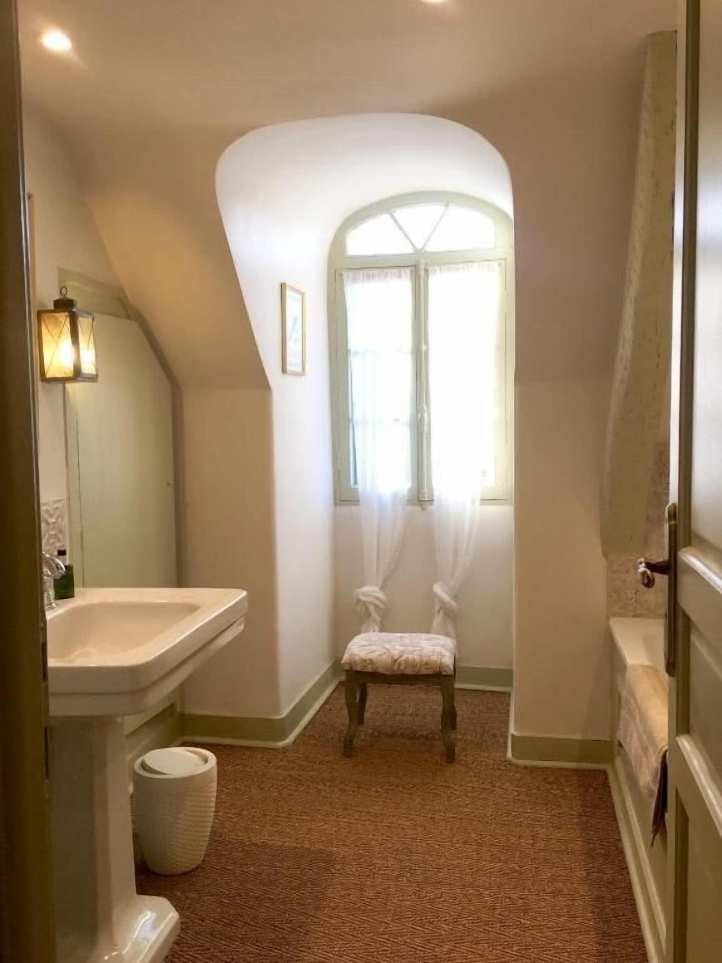 Une salle de bain avec un lavabo, une chaise, une fenêtre et une porte.