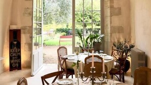 A dining area with a table set for four, a chandelier, and a view through a large arched window. - Le Gaimont (Vouvray)