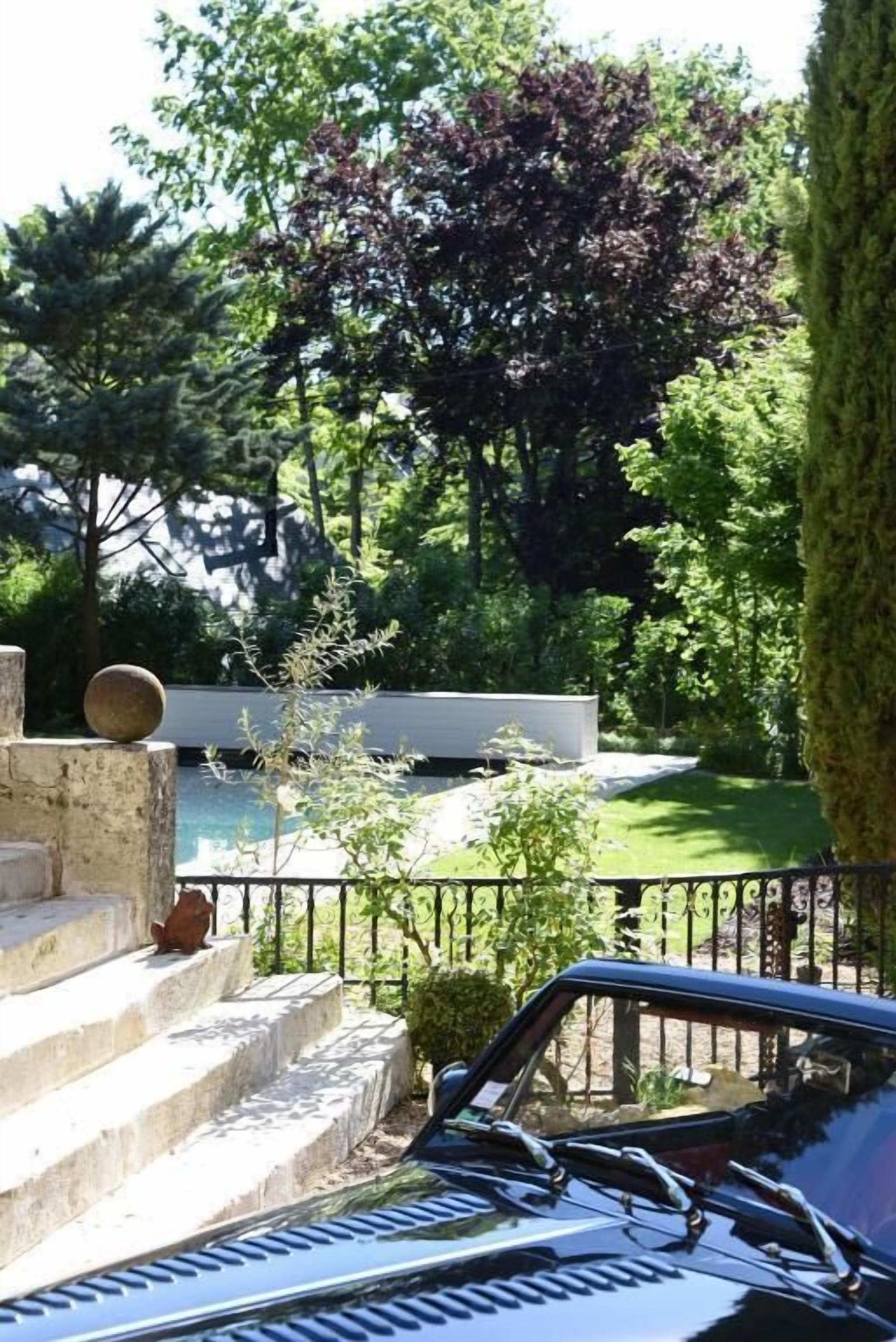 A car parked in front of a stone staircase leading to a pool area surrounded by lush greenery and trees.