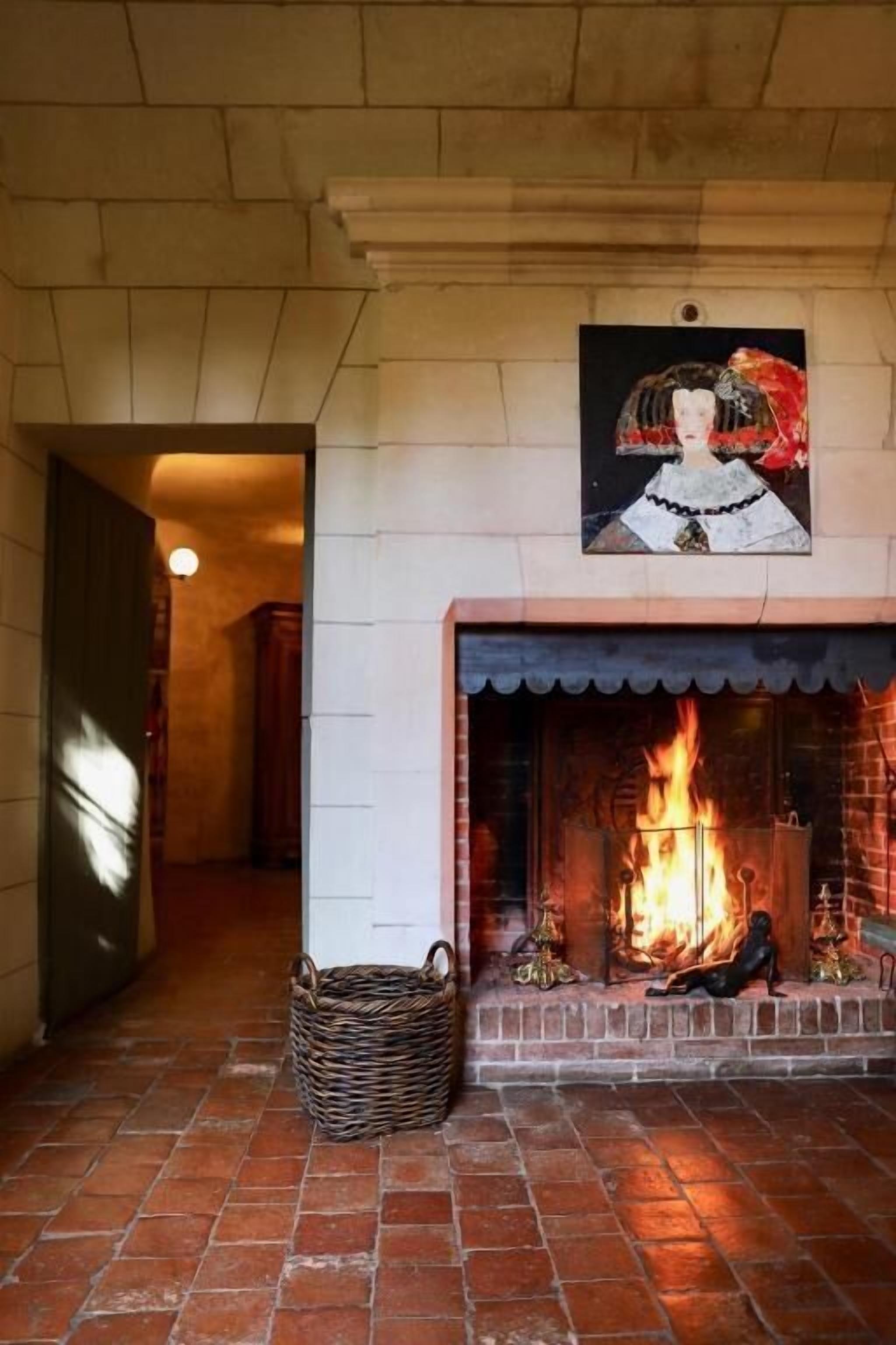 Une cheminée avec un feu crépitant, un panier en osier et un tableau accroché au mur.
