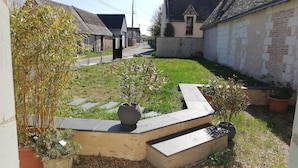 Une cour avec un chemin pavé, des plantes en pot et un petit espace aménagé en jardin.