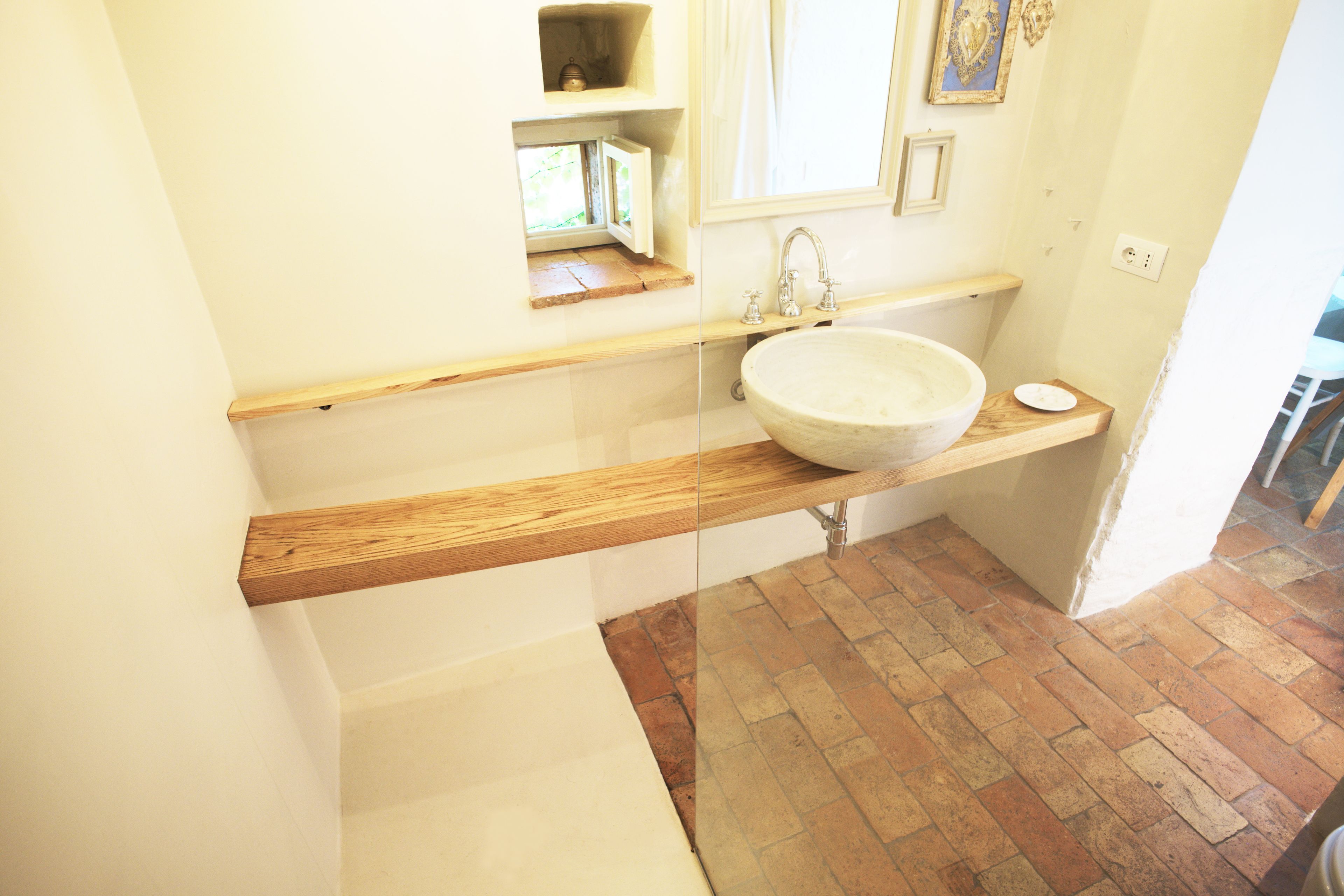 A bathroom with a wooden vanity, a large round sink, and a window with a view of greenery.