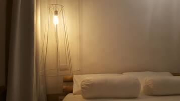 Una cama con sábanas blancas y una lámpara de pie moderna con una bombilla.