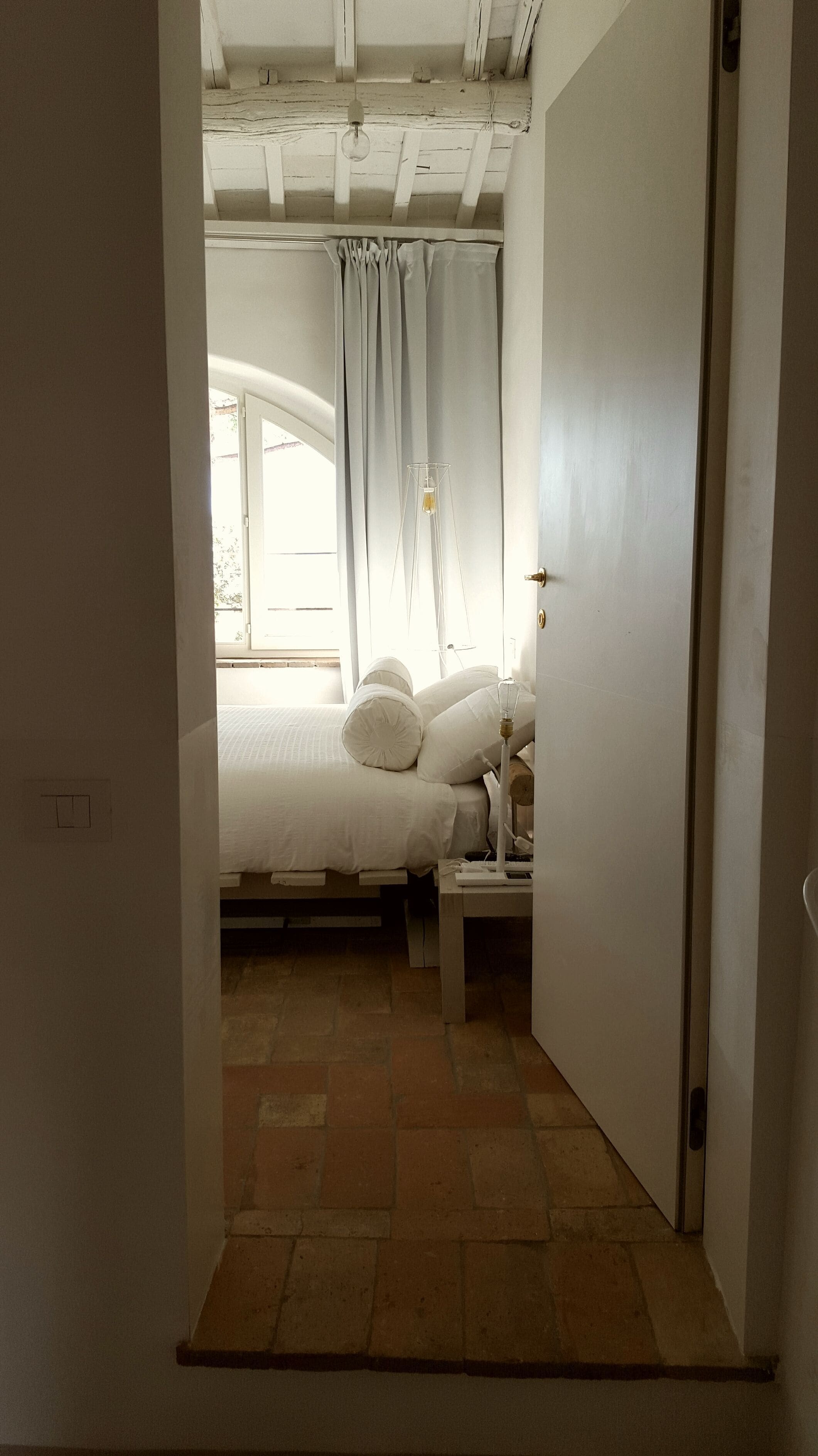 Un dormitorio con cama, mesita de noche, lámpara y ventana con cortinas.