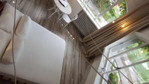 A modern hotel room with a large bed, a round table with chairs, and a view of a garden through large windows. - B&B A Piazza del Gesù (Viterbo)