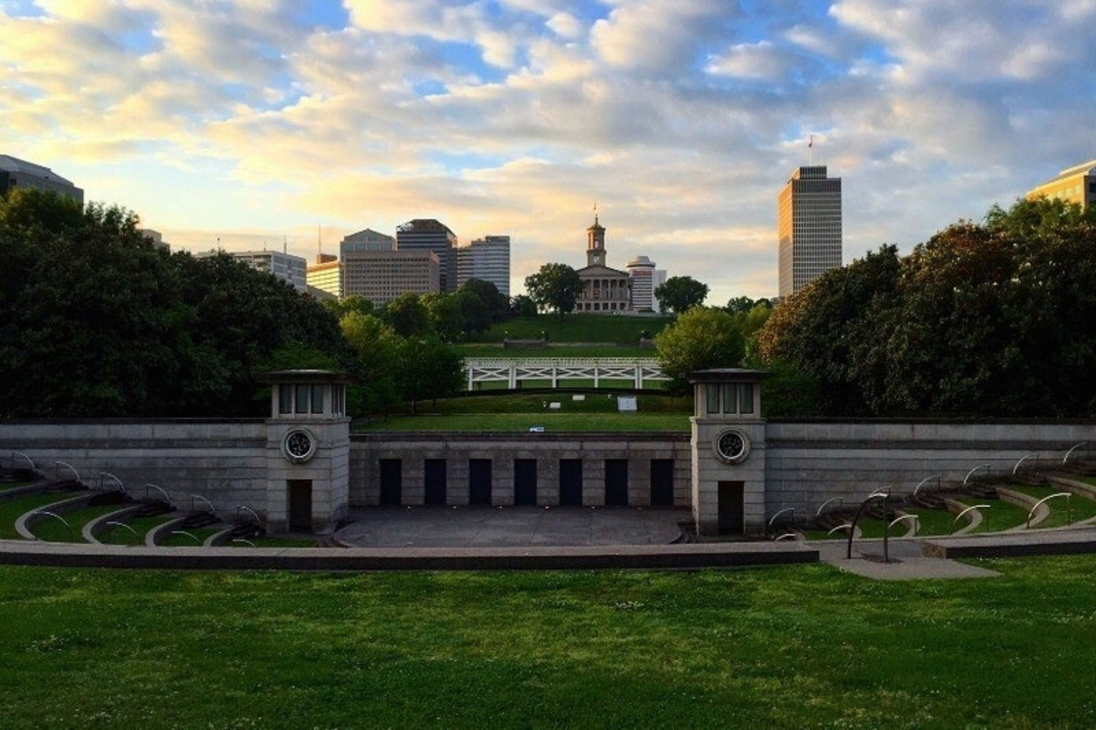 Un parc avec une pelouse centrale, un bâtiment doté d’une tour horloge et, au loin, un gratte-ciel moderne.