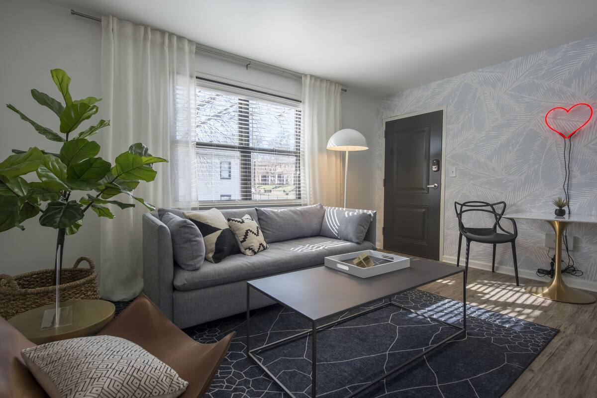 Een moderne woonkamer met een grijze bank, een bijzettafeltje, een potplant en een lamp.