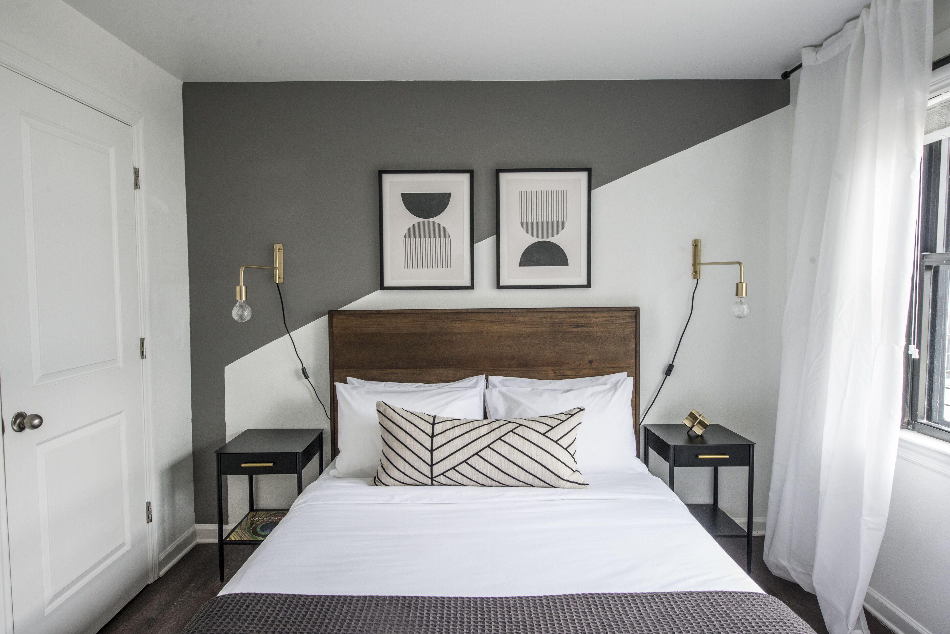 Un dormitorio ordenado con una cama grande, dos mesitas de noche, un cabecero y dos lámparas fijadas a la pared.