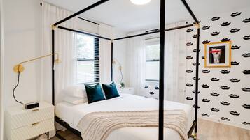 A four-poster bed with a white canopy, a bedside table with a lamp, and a wall with a pattern of lips.
