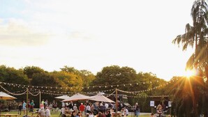 Un événement en plein air où les participants sont assis à des tables sous des parasols, entourés de verdure et d’une guirlande de lumières.