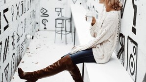 Une personne est assise sur un banc dans une pièce dont les murs sont recouverts de divers dessins et symboles en noir et blanc.