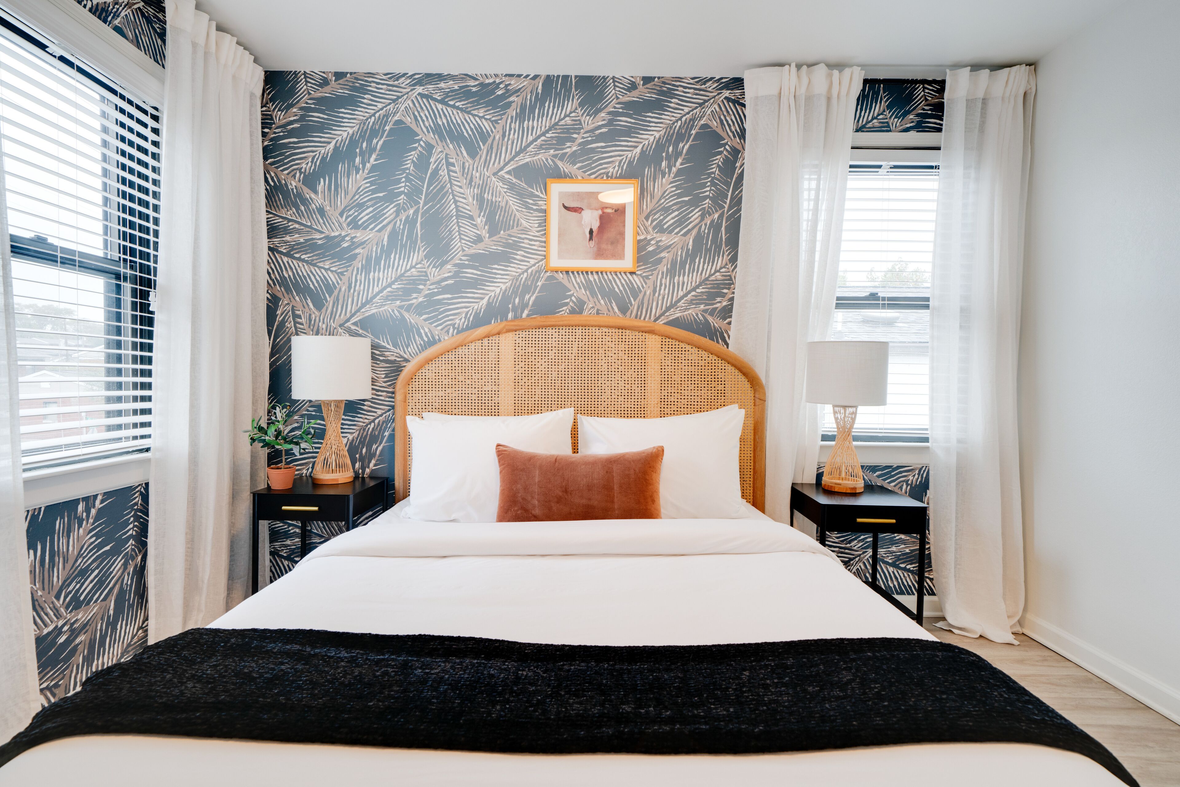 A neatly made bed with white and brown bedding, flanked by two nightstands with lamps and a potted plant.