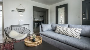 Un salon moderne avec un canapé gris, un fauteuil à armature métallique noire, une table basse noire et un panier décoratif.