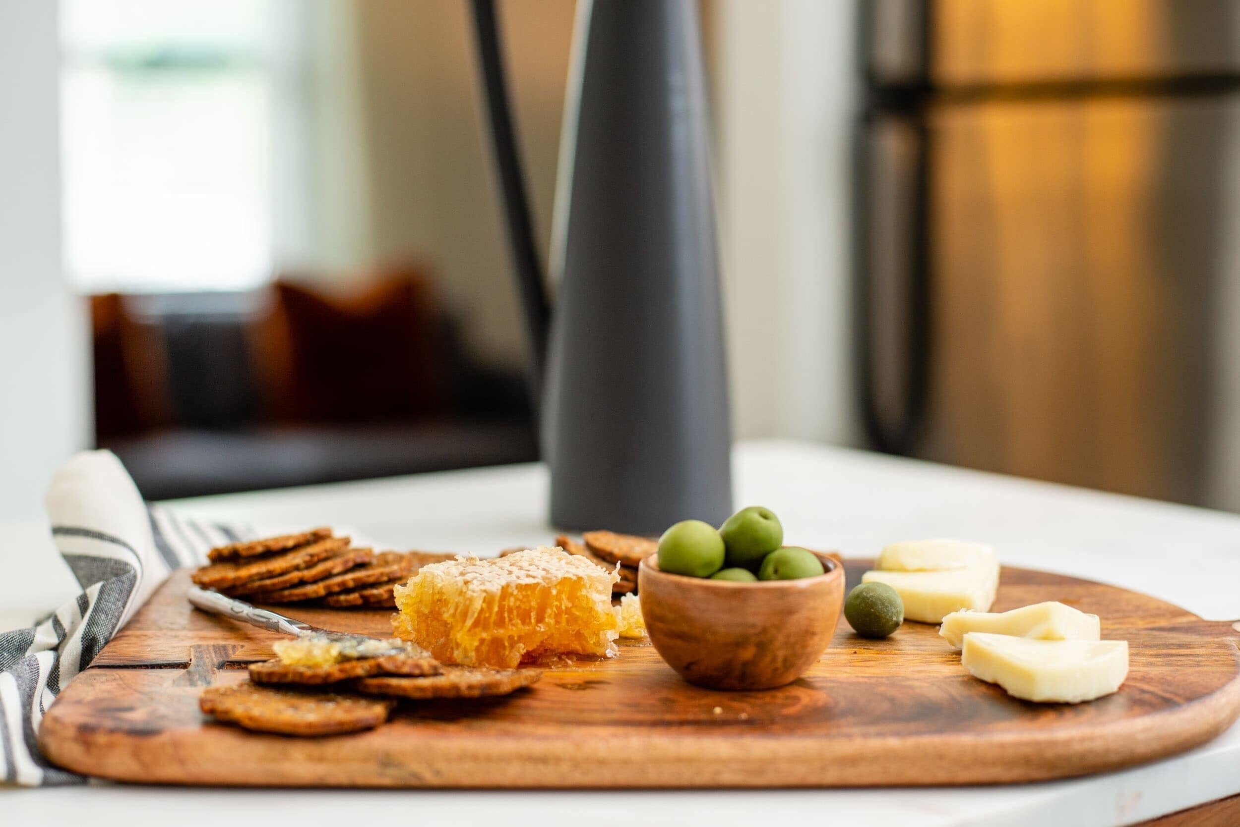 Ein Holzboden mit Crackern, Bienenhonig, grünen Oliven und Käse auf einem Tisch.