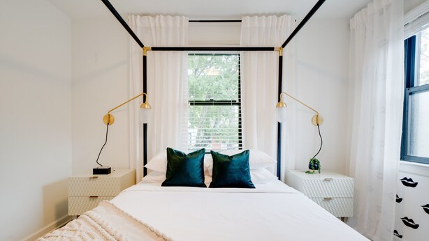 Une chambre moderne avec un grand lit, des murs blancs et une fenêtre équipée de stores.