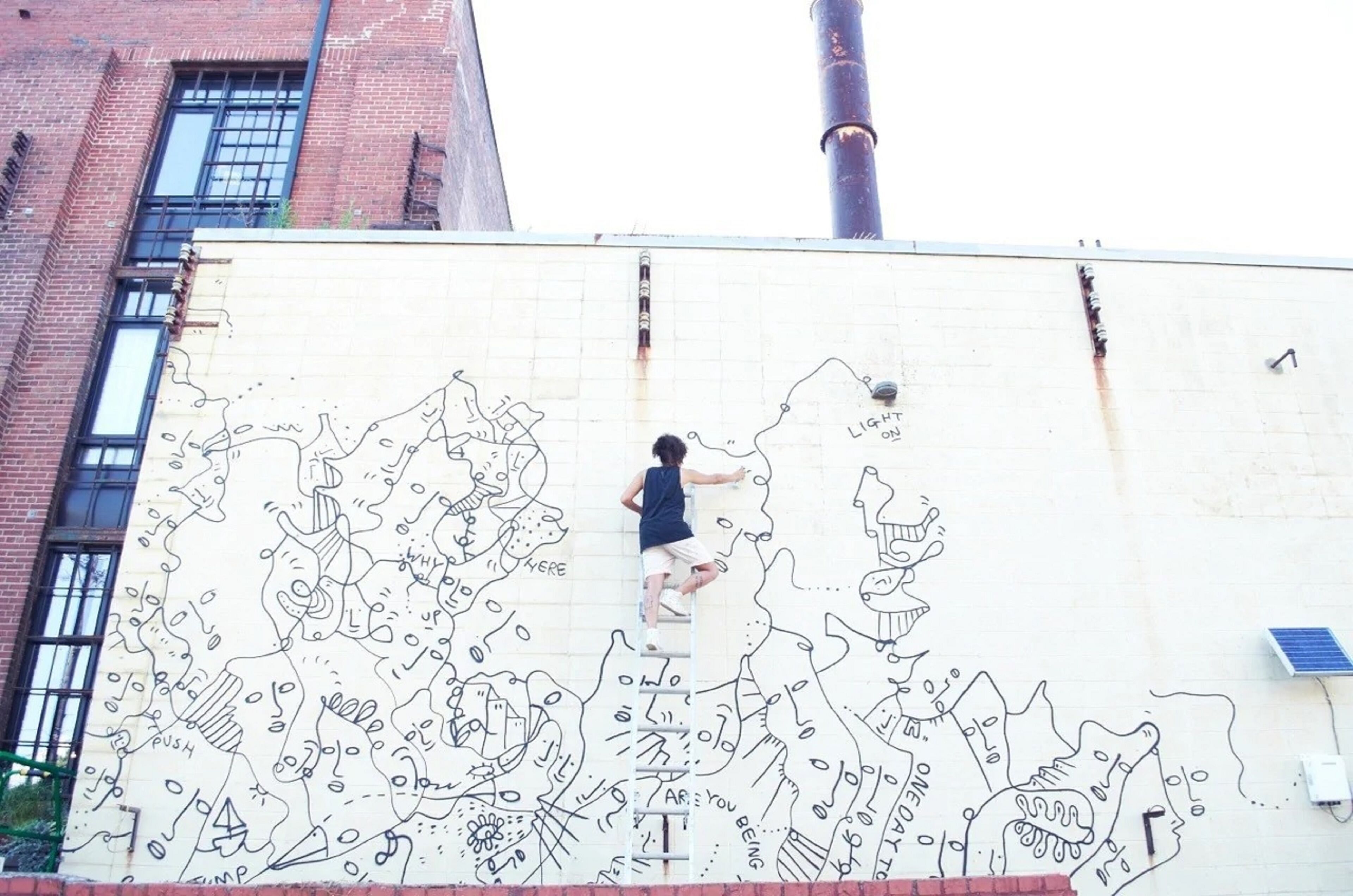 Una persona sube una escalera para pintar un mural en la pared de un edificio.