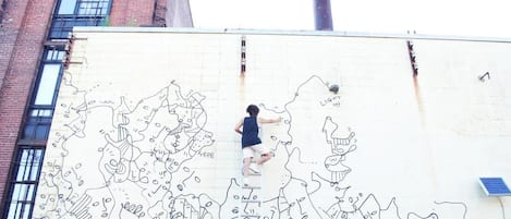 Una persona sube una escalera para pintar un mural en la pared de un edificio.