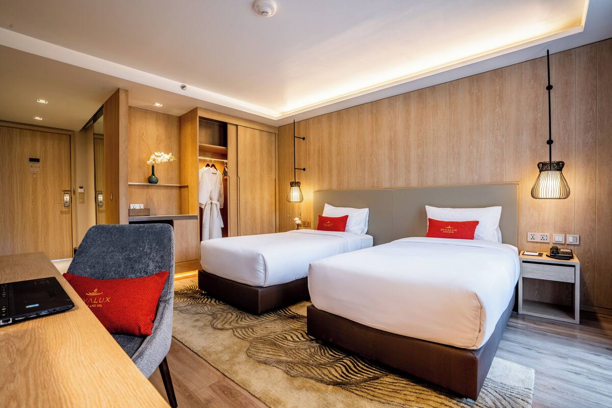 A hotel room with two beds, a desk, a chair, a wardrobe, and a nightstand.