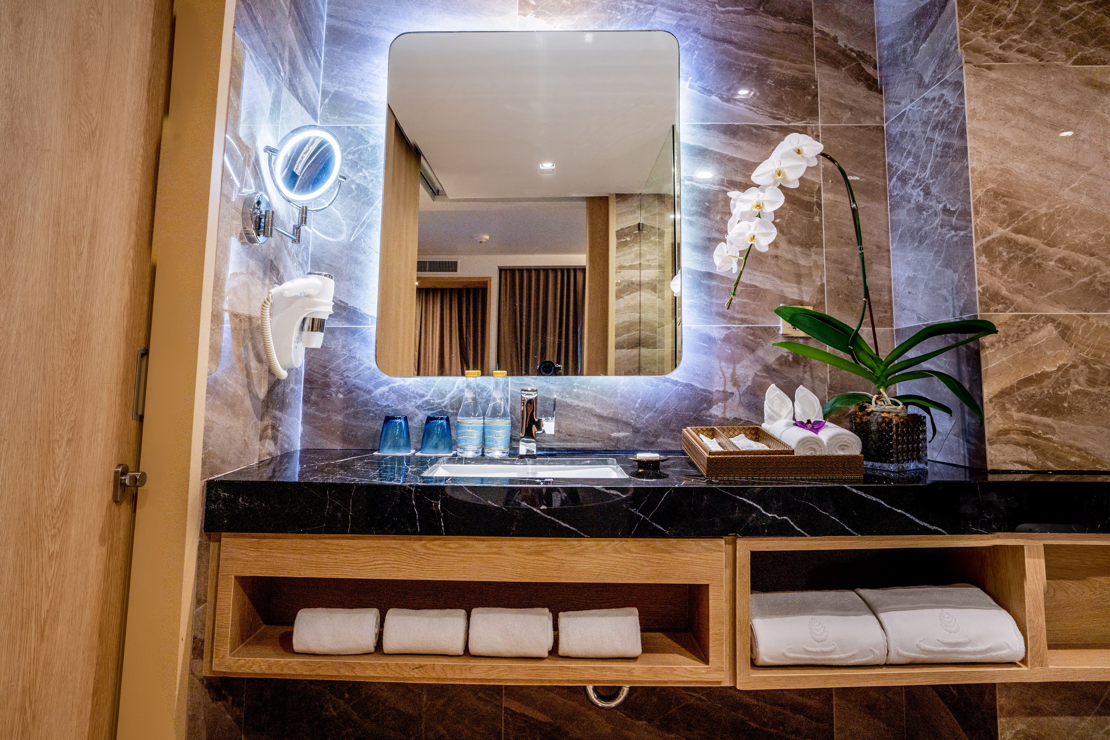 A bathroom with a marble sink, a mirror, a hairdryer, and a potted orchid.