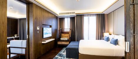 Una habitación de hotel moderna con una cama grande, una zona de estar, un televisor y piso de madera.
