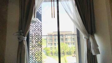 A room with a large window, curtains, and a view of a building and greenery outside.