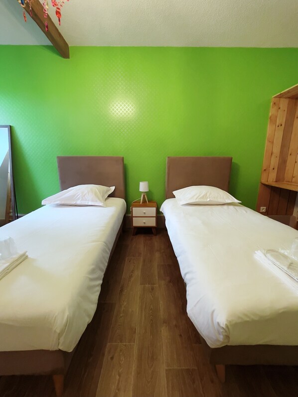 A room with two beds, a wooden nightstand with a lamp, and a green wall.