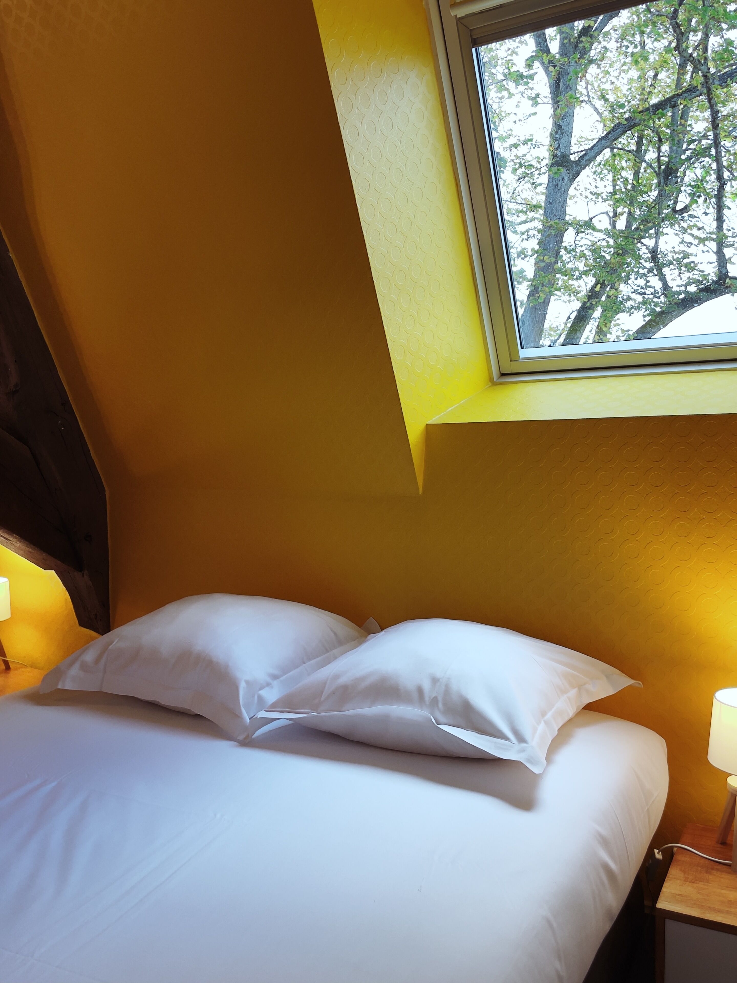 Un dormitorio con una cama, dos lámparas de noche y una ventana con vistas a árboles.