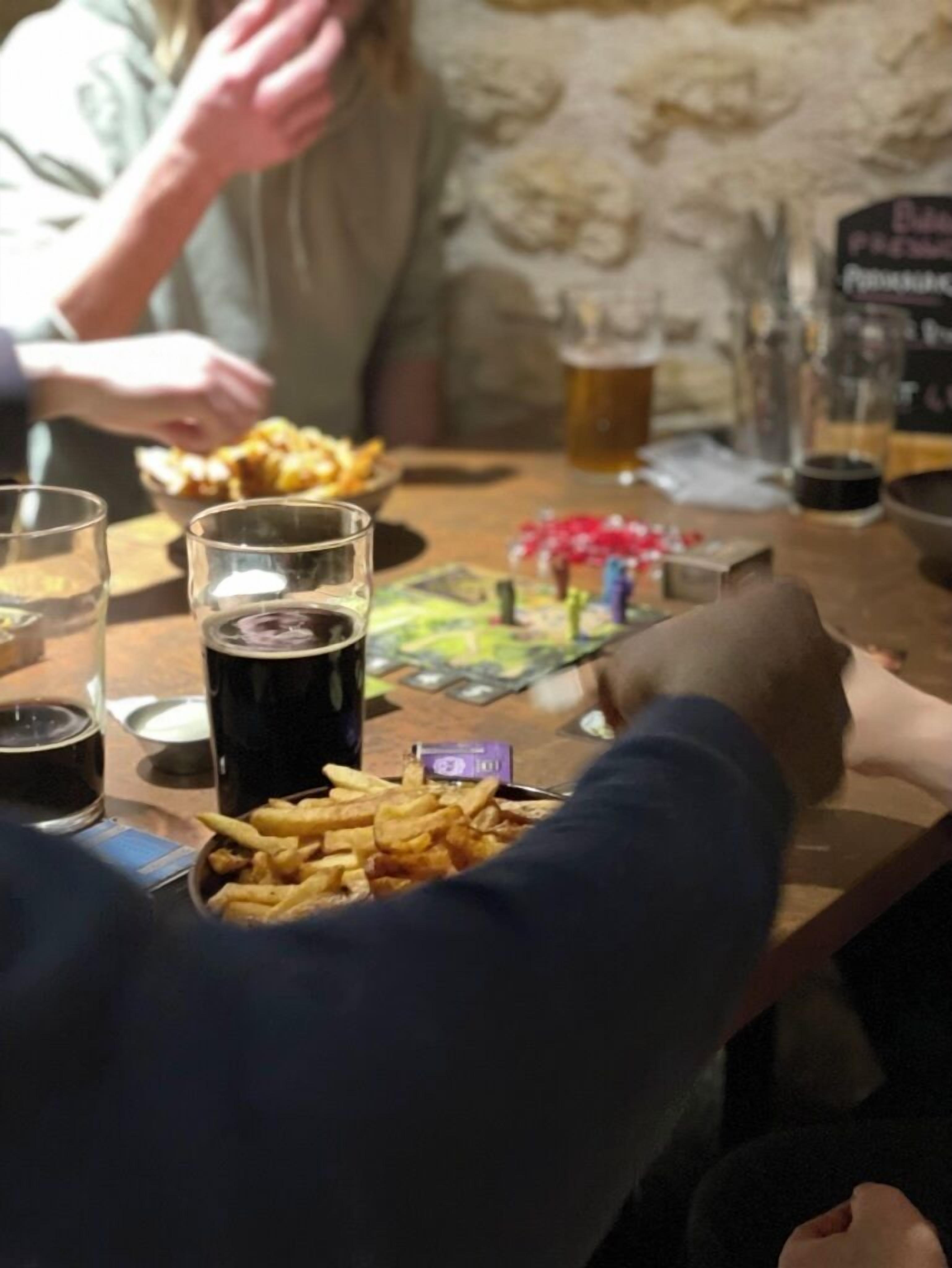 Una mesa con papas fritas, una cerveza oscura y un juego de cartas.