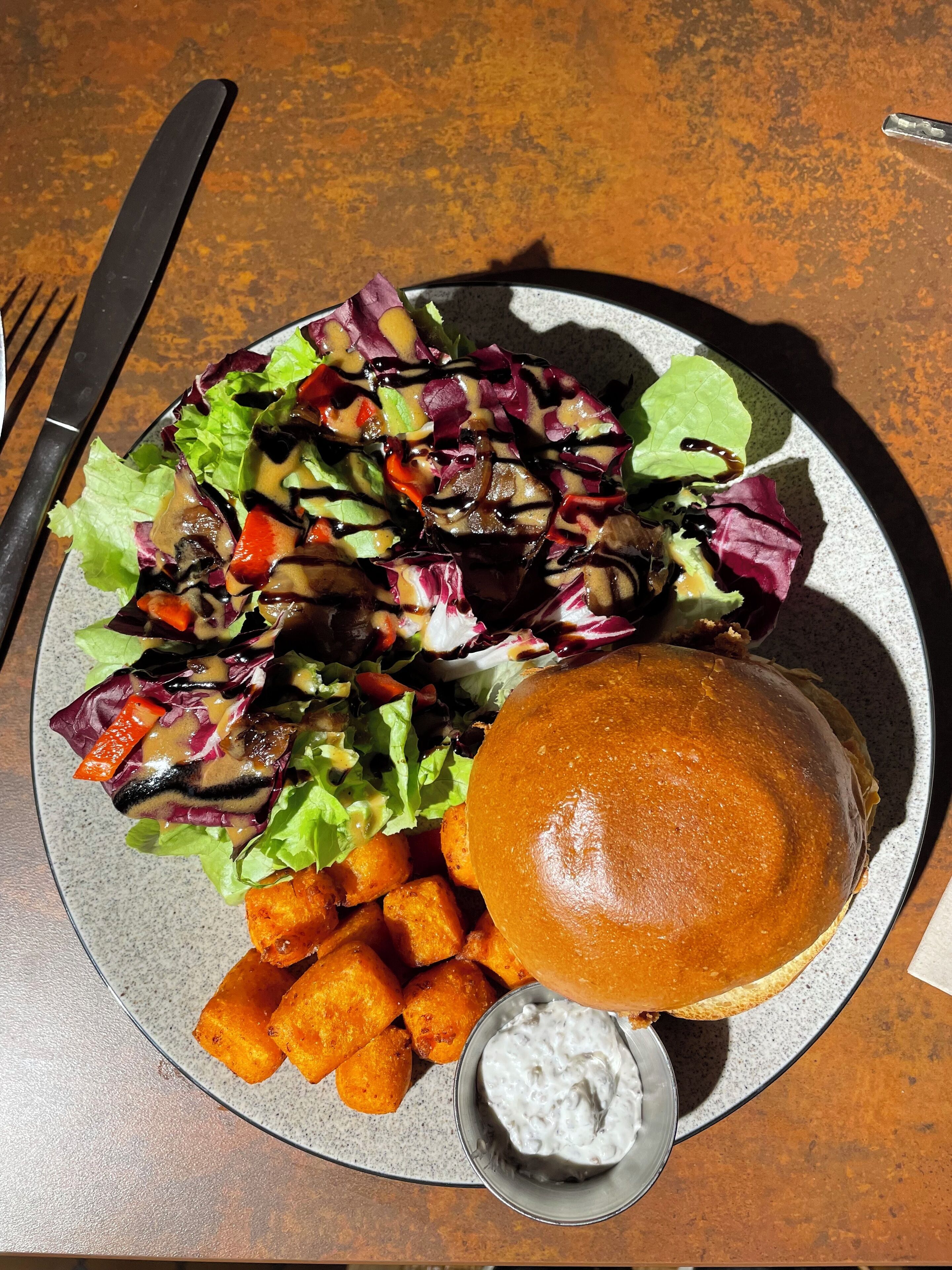 Un plato con una hamburguesa, una ensalada pequeña y un recipiente con salsa.