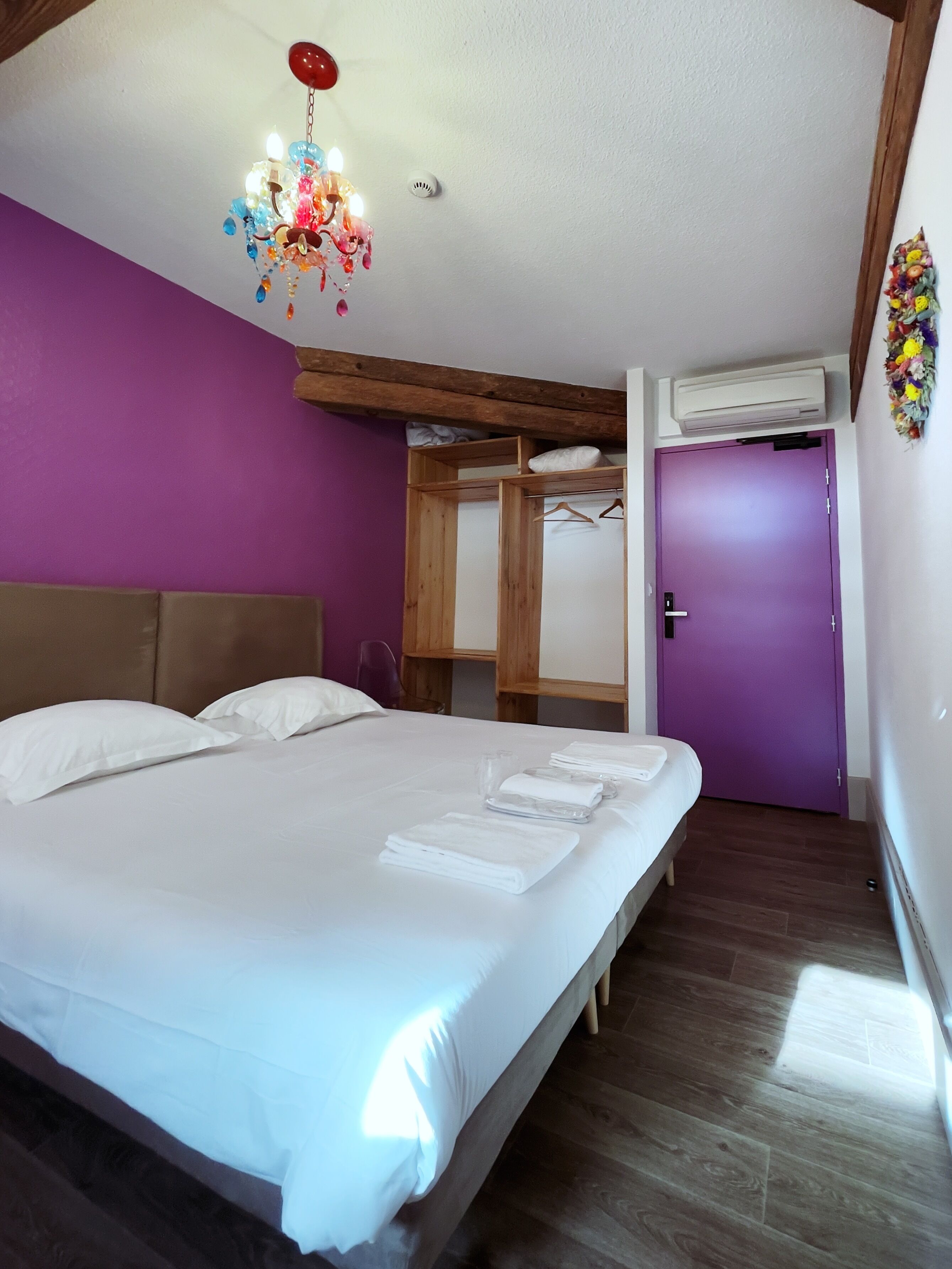 Un dormitorio con una cama grande, cabecera de madera, paredes moradas, una lámpara en el techo y un equipo de aire acondicionado.