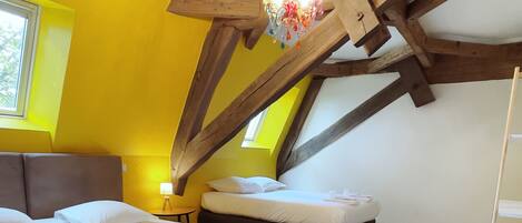 A bedroom with two beds, wooden beams, a chandelier, and a window.