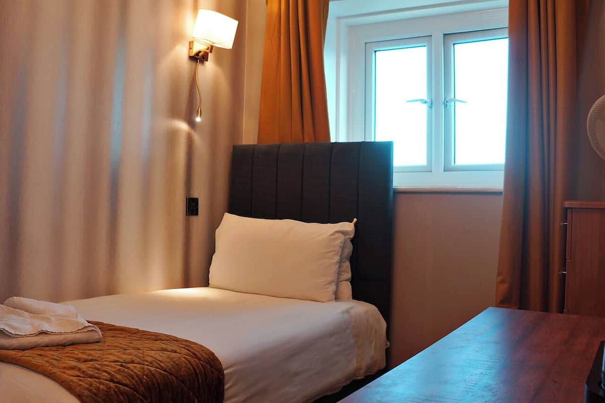 A hotel room with a bed, a bedside table, a lamp, and a window with curtains.