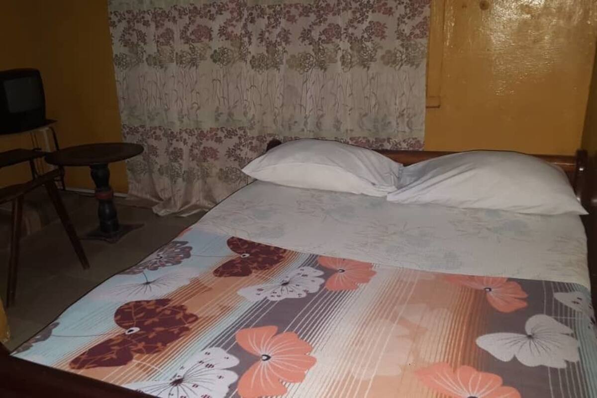 Una habitación con una cama, una silla, una mesita y un televisor.