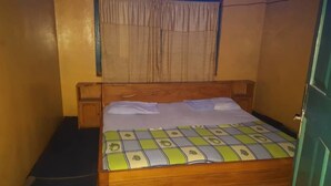 A single bed with a patterned bedspread, a wooden headboard, and a window with curtains. - Topway Hotel (Nkawkaw)