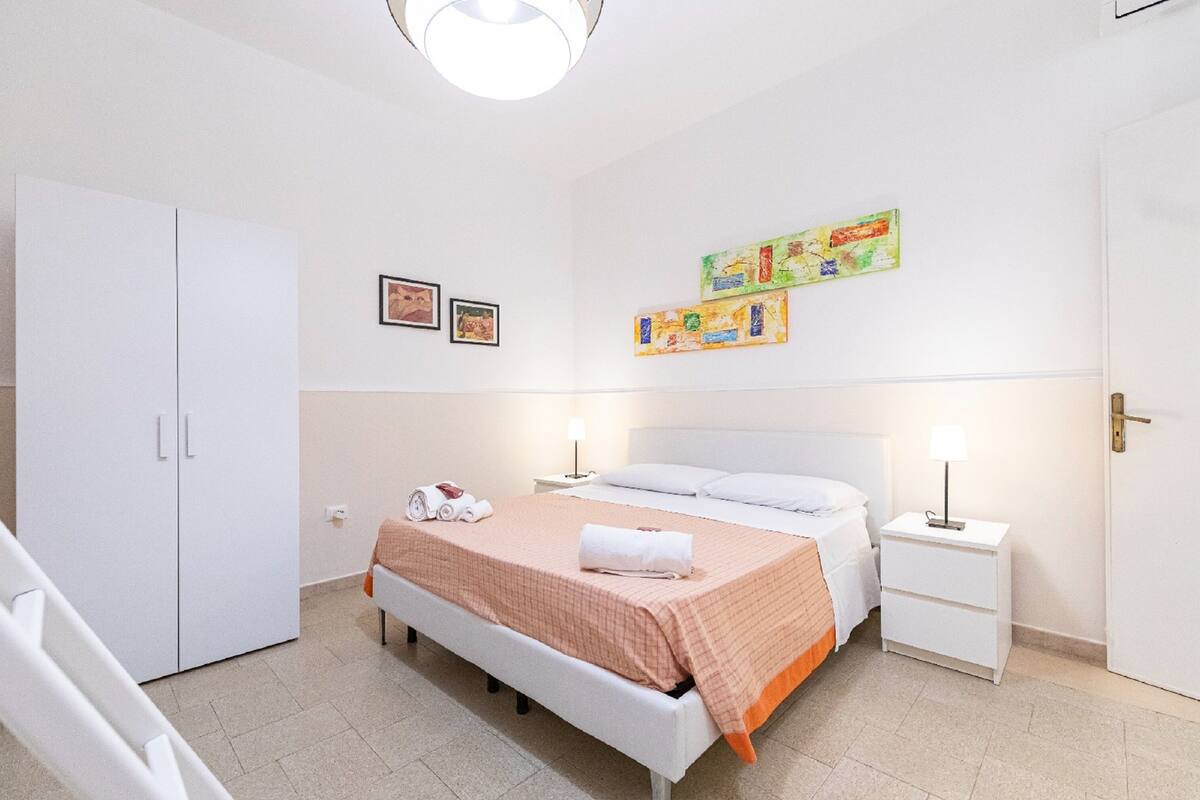 Un dormitorio con cama, mesitas de noche, armario y cuadros en la pared.