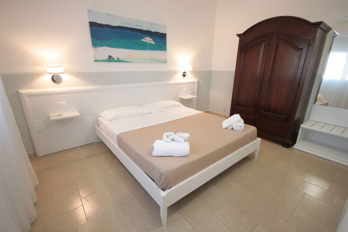 Un dormitorio con cama, mesitas de noche, un armario de madera y un cuadro en la pared.