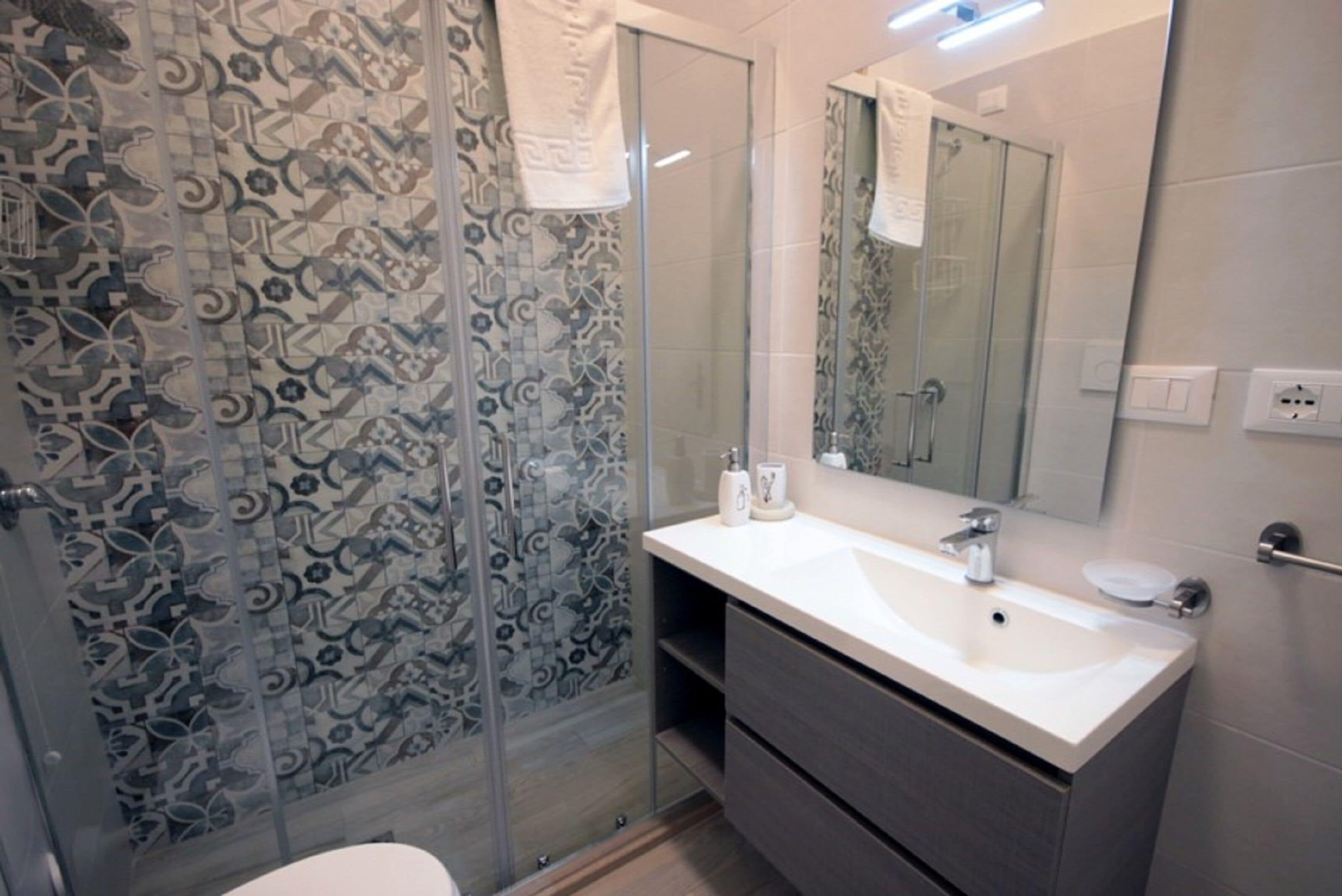 A bathroom with a glass shower enclosure, a white sink with a mirror above it, and a towel hanging on the shower door.