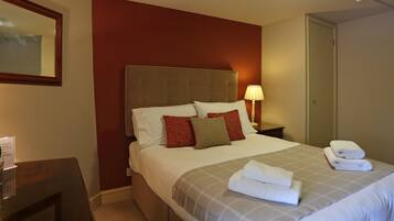 A hotel room with a large bed, a nightstand with a lamp, a mirror, and a door.