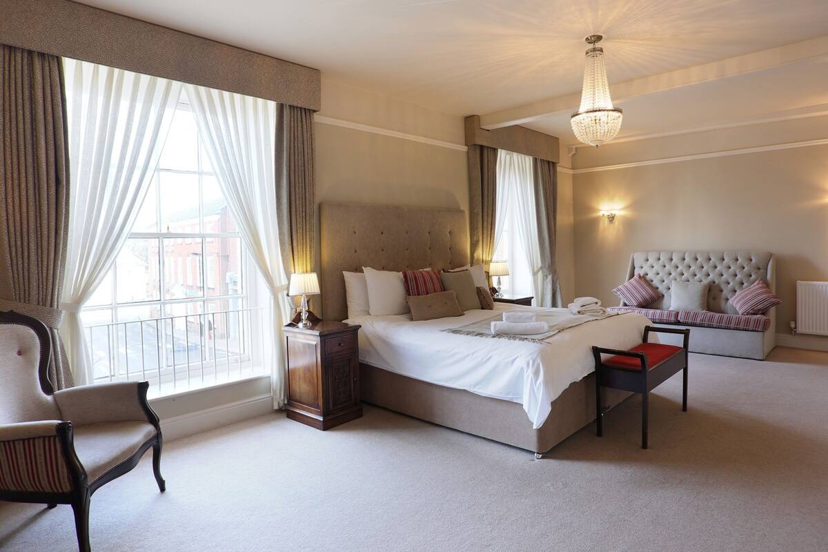 Een goed verlichte hotelkamer met een groot bed, een nachtkastje, een stoel en een bank.