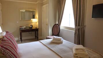 Une chambre d’hôtel avec un lit, un bureau, une chaise, un miroir et une fenêtre avec des rideaux.
