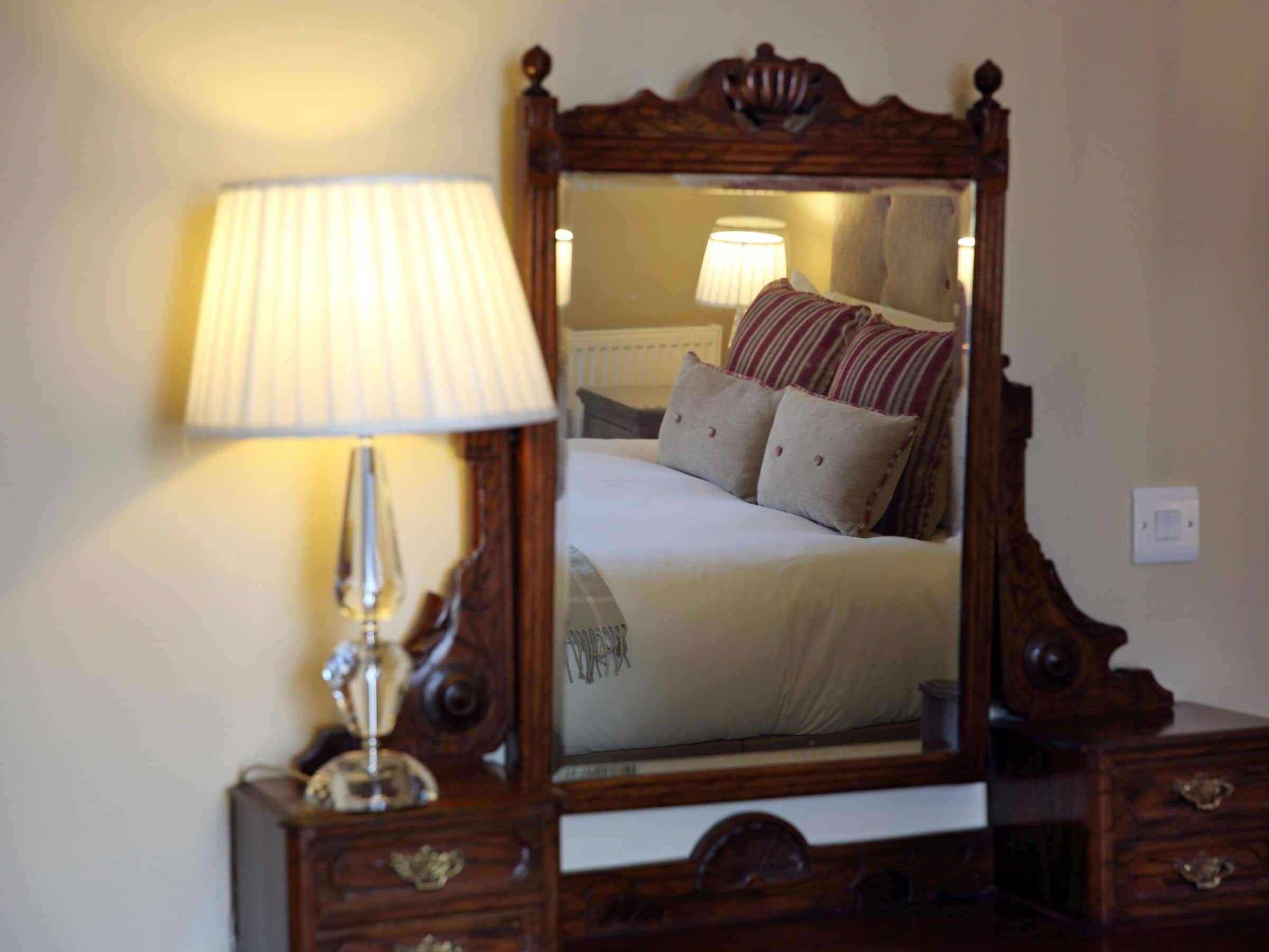 A bedroom with a wooden dresser, a mirror, a lamp, and a bed with pillows.