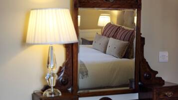 A bedroom with a wooden dresser, a mirror, a lamp, and a bed with pillows.