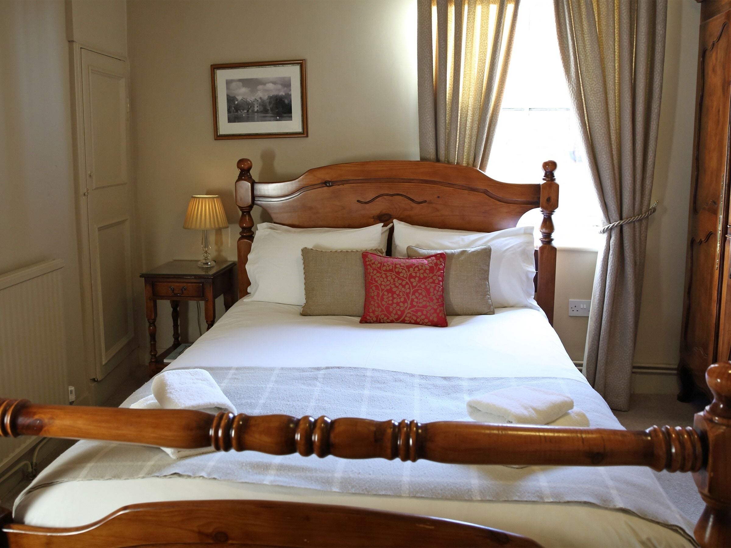A neatly made bed with a wooden headboard, a bedside table with a lamp, and a framed picture on the wall.