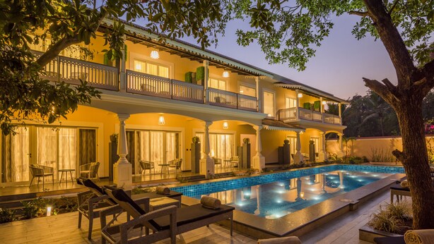 A two-story hotel with a swimming pool, outdoor seating, and a well-lit balcony. - Maravilha a boutique stay (Assagao)