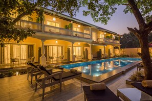 Un hotel de dos pisos con piscina, mobiliario exterior e iluminado balcón.