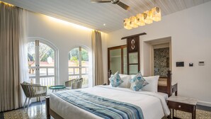 A hotel room with a large bed, a sitting area with a chair, a small table, and a ceiling fan. - Maravilha a boutique stay (Assagao)