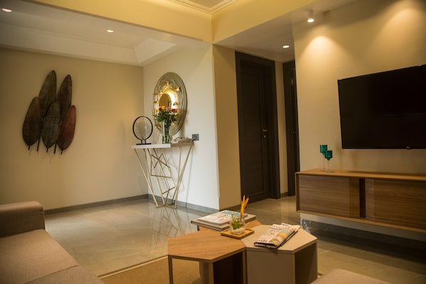 A modern living room with a sofa, a coffee table, a TV, and a decorative mirror. - Fazlani Nature's Nest – Your Pathway to Wellness Retreat (Mawal)