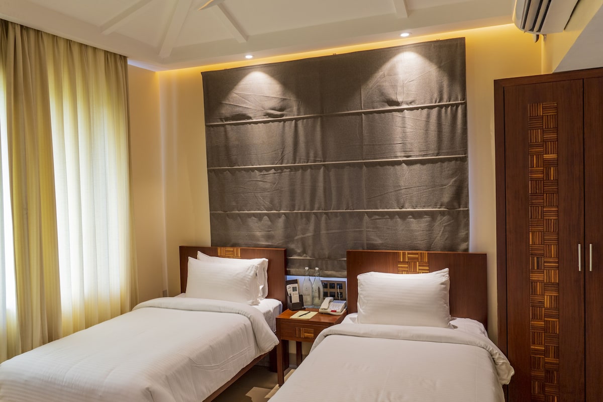 Une chambre d’hôtel avec deux lits, une grande œuvre d’art accrochée au mur et une armoire en bois.