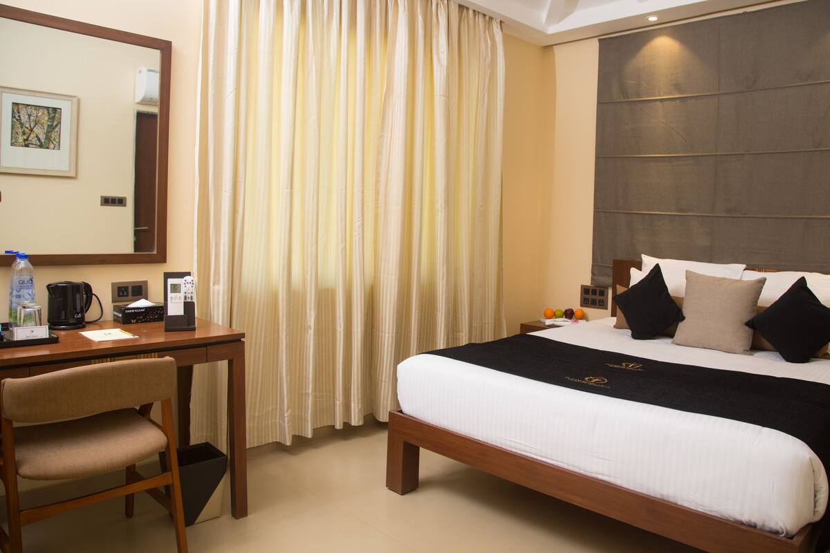 Une chambre d’hôtel avec un lit, un bureau, une chaise, un miroir et une fenêtre avec des rideaux.
