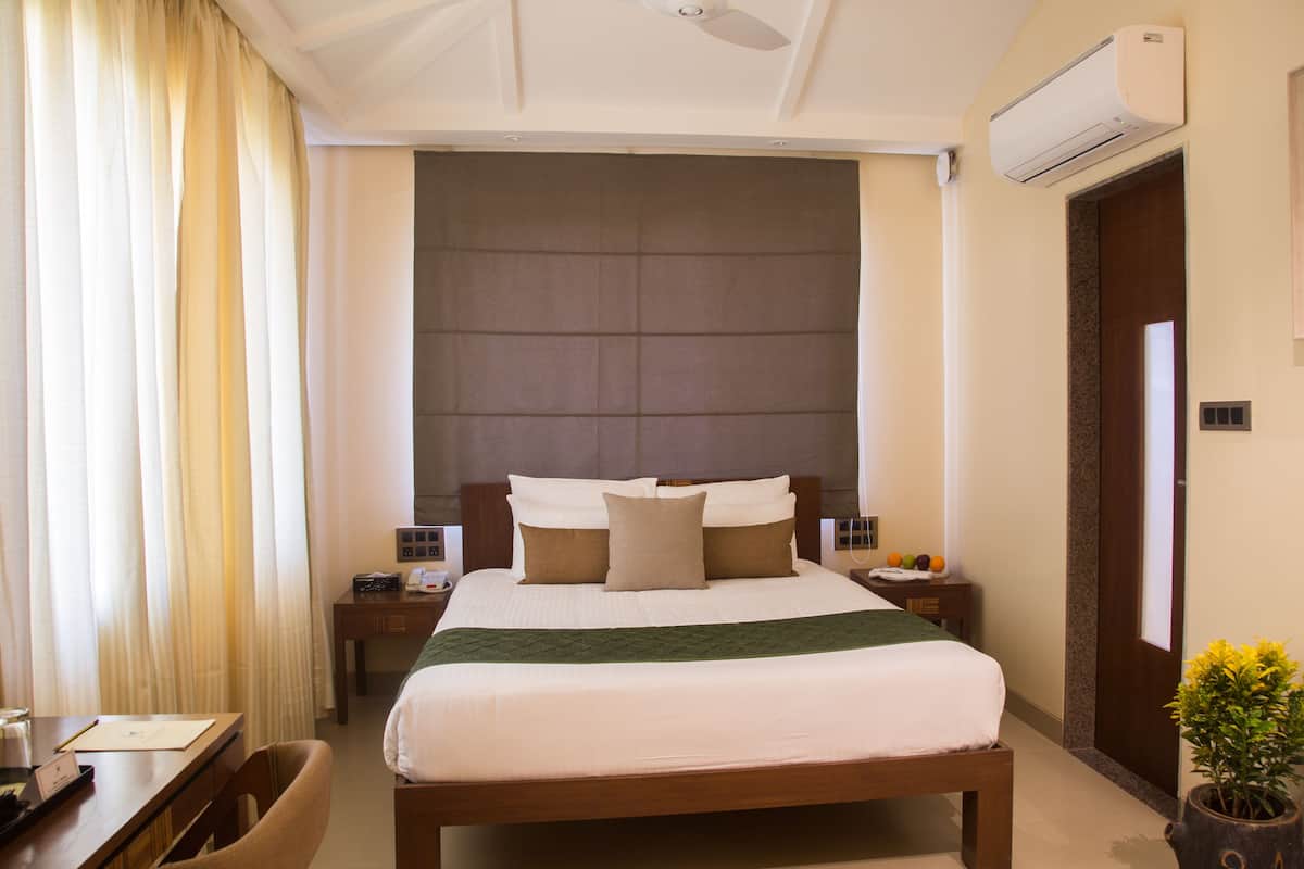 Une chambre d’hôtel avec un grand lit, un bureau avec une chaise, une table de chevet, un climatiseur fixé au mur et une porte.